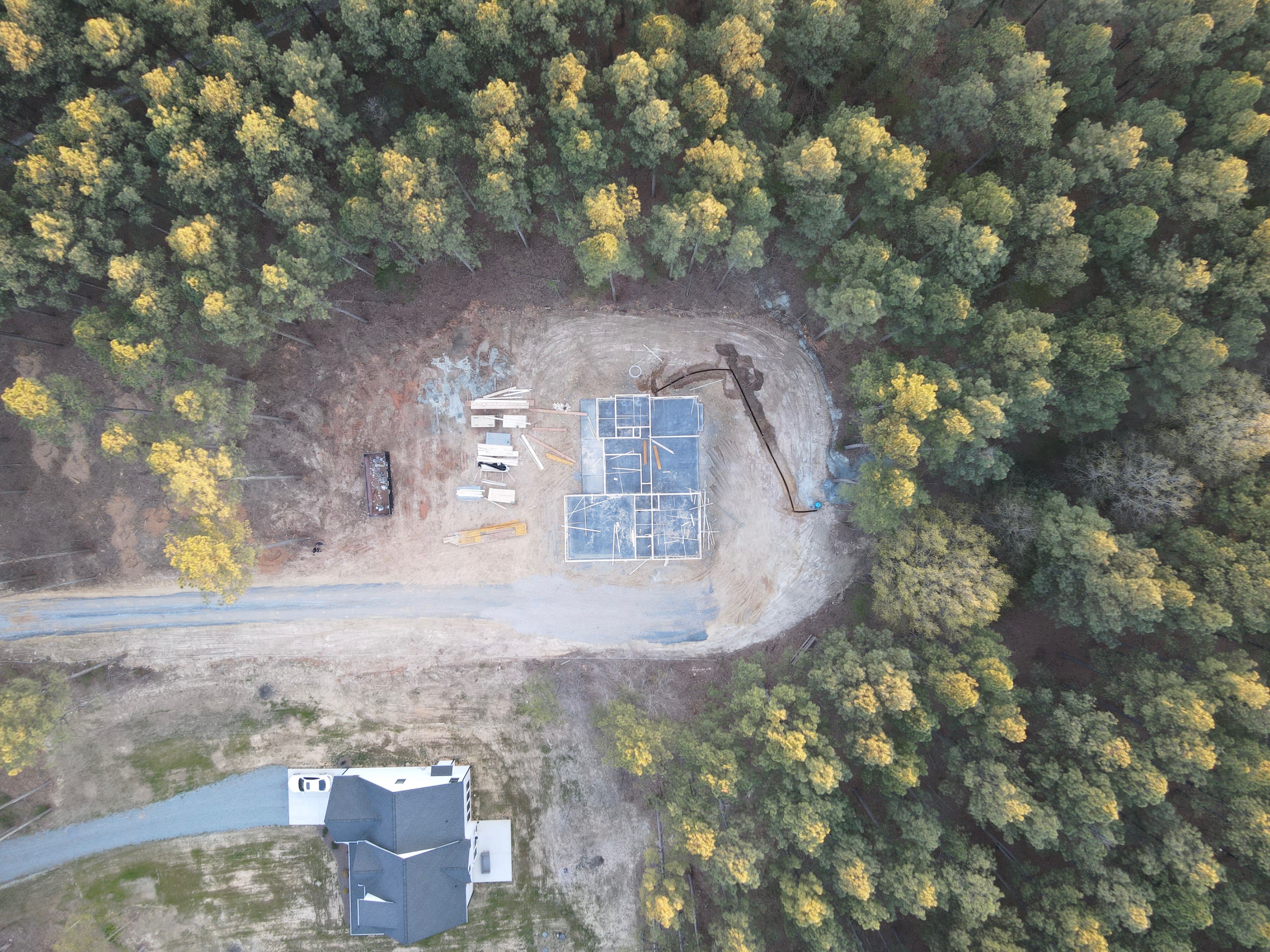Aerial view of new home construction site with foundation work surrounded by forest.