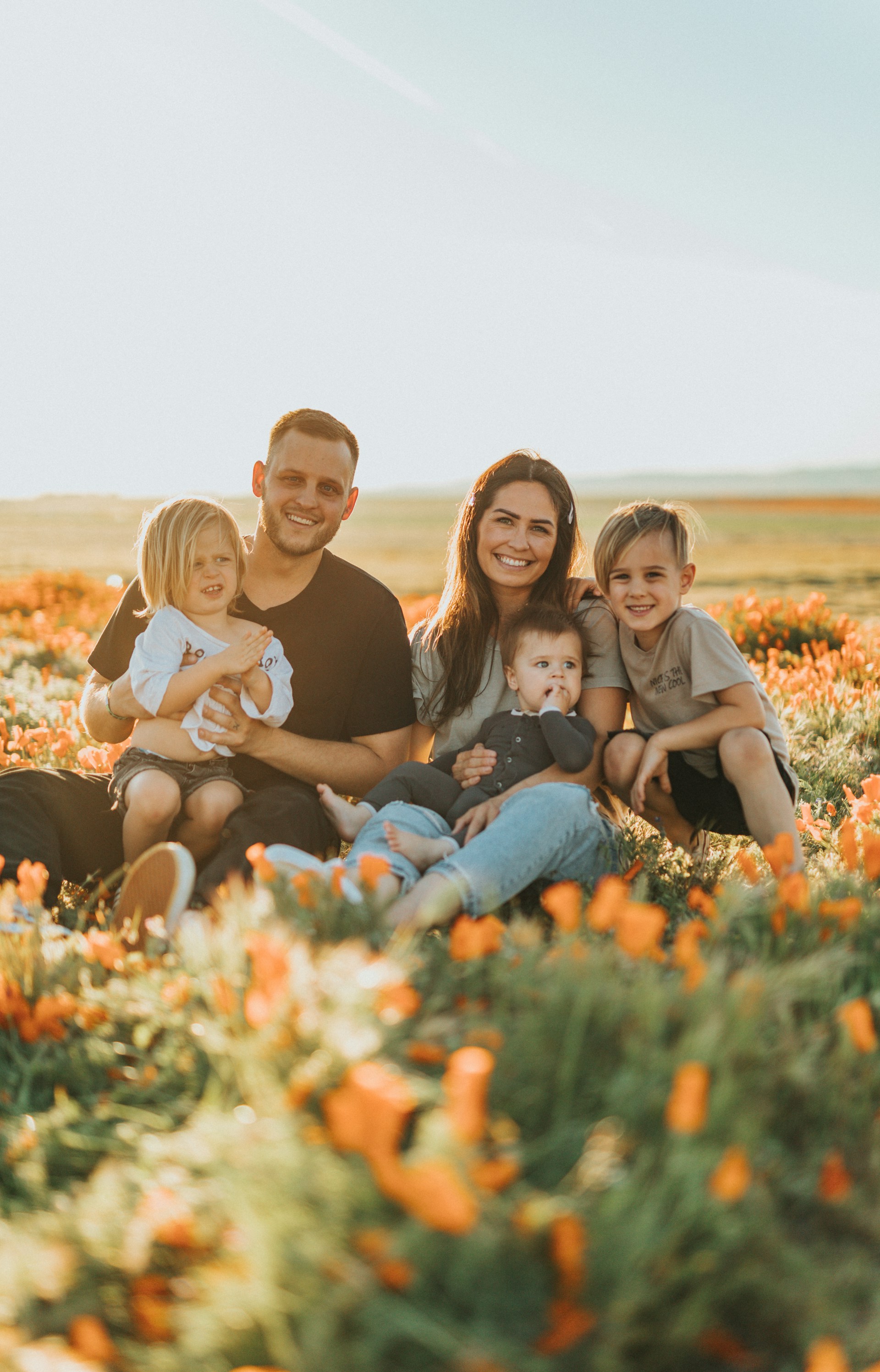 Smiling family of five sitting together in a flower field at sunset.