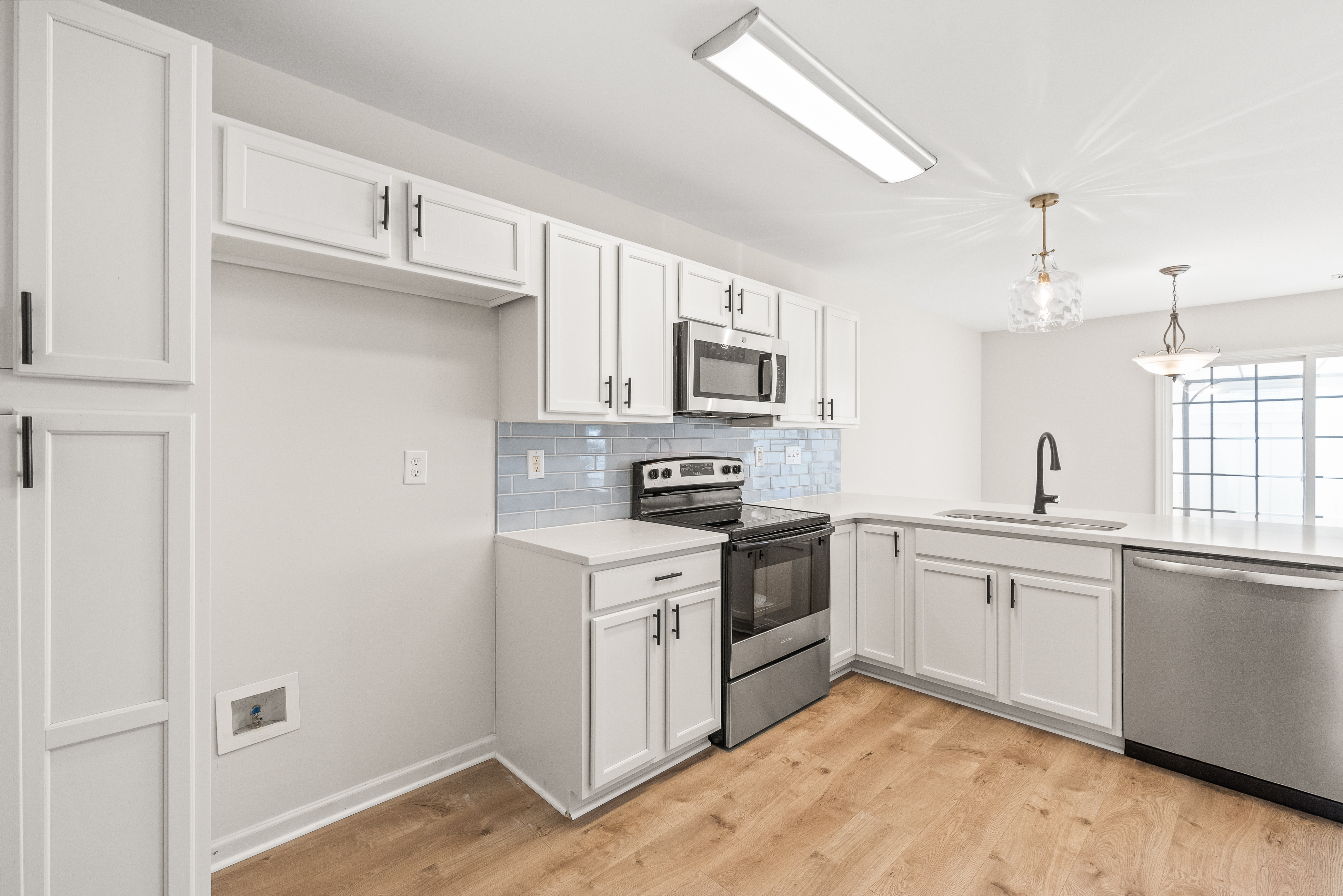 Renovated kitchen with white cabinets, stainless steel appliances, light wood flooring, and blue subway tile backsplash.
